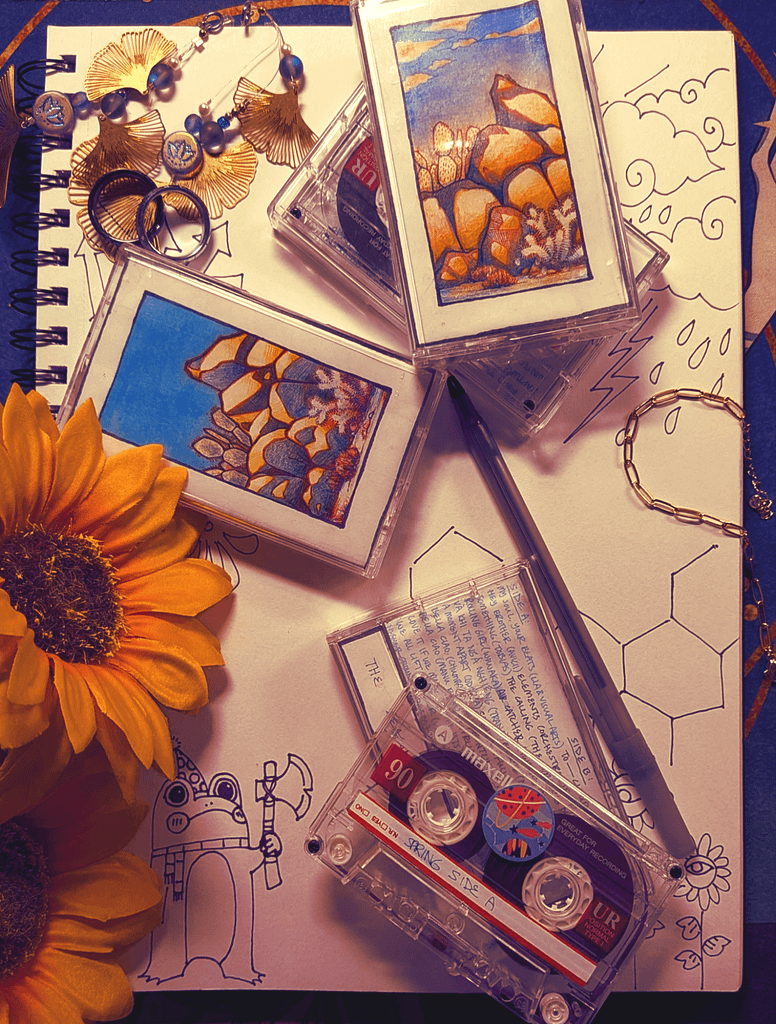 Cassette tapes and sunflowers scattered on a page of sketches. A frog is holding a handaxe.